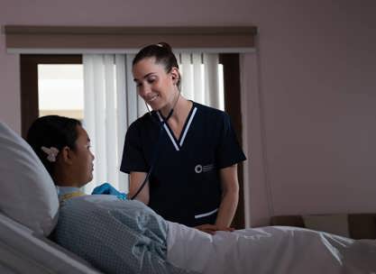 A nurse caring for a patient in a hospital room while comparing Long-Term Care Facility vs Nursing Home services.